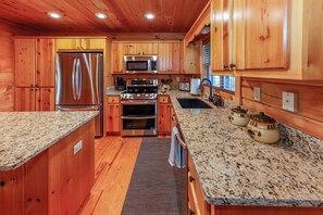 A kitchen with wooden cabinets, stainless steel appliances, granite countertops, and a window with blinds. - Game Room  / Mtn Views  / Hot Tub / Fire Pit & Fire Table /  Coffee Bar / (Lake Lure)