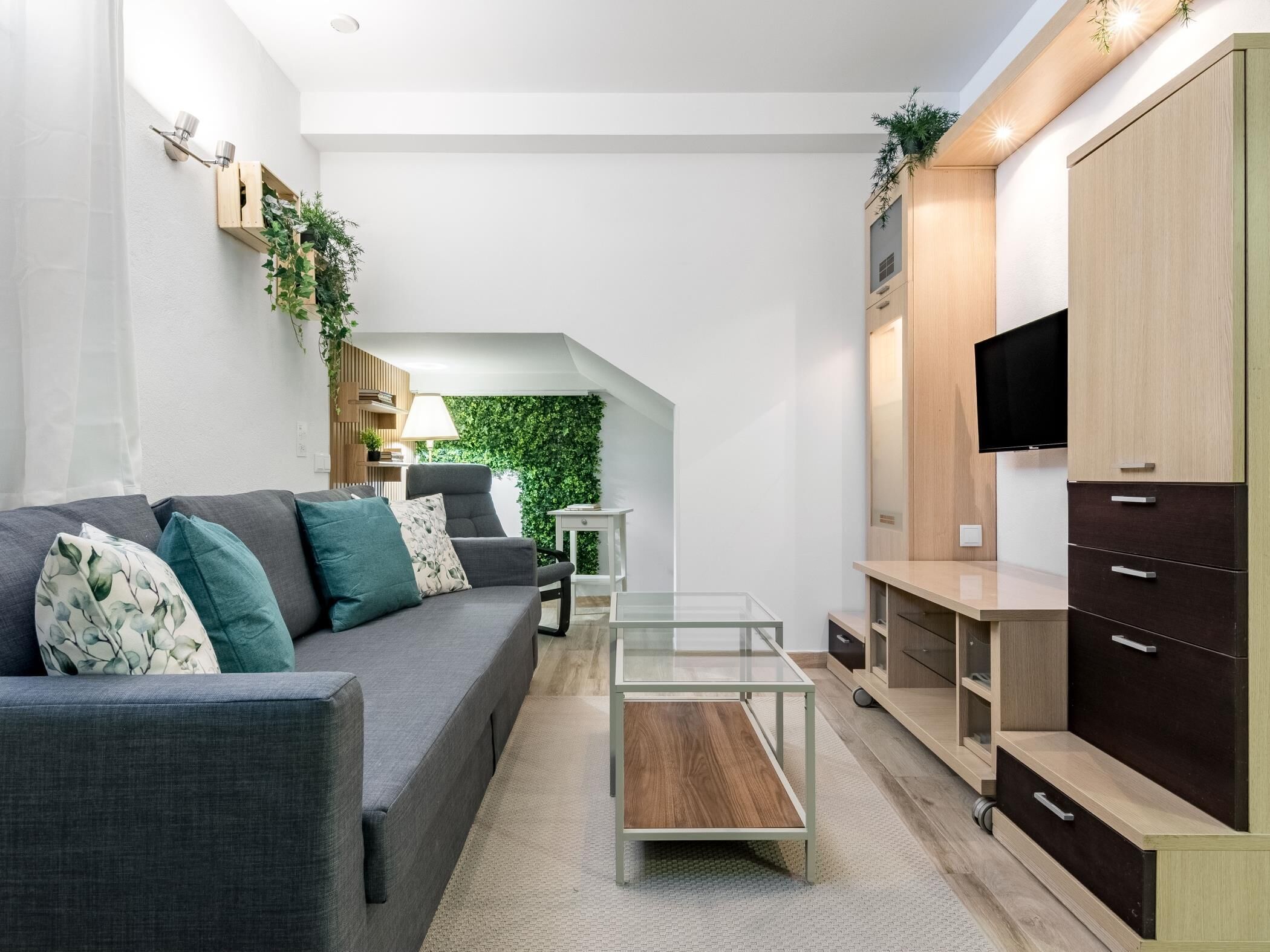 A modern living room with a grey sofa, a glass coffee table, and a TV mounted on a wooden cabinet.
