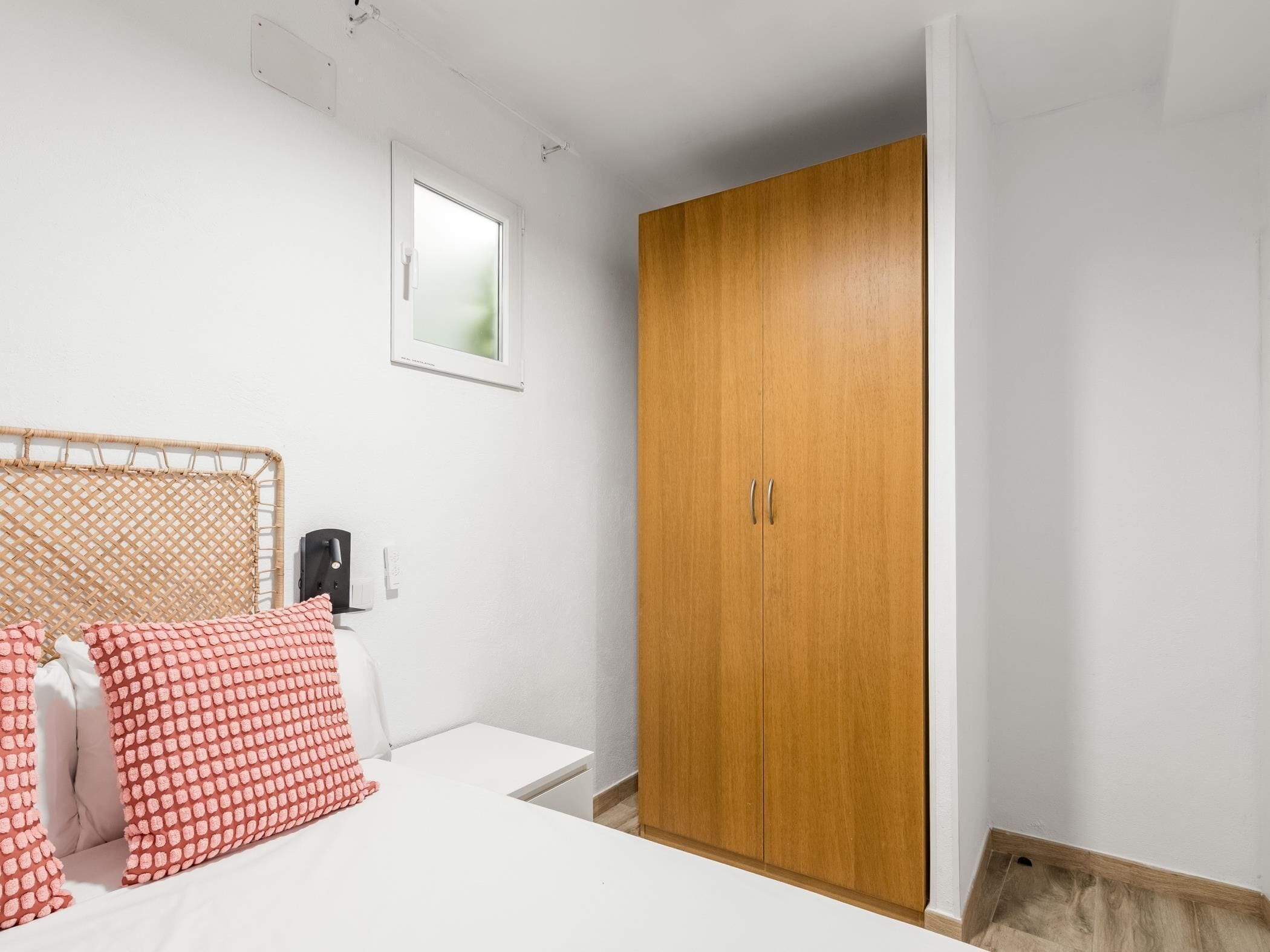 A bedroom with a bed, a wooden wardrobe, and a small window.