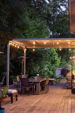 Une terrasse extérieure dotée d’une pergola, de guirlandes lumineuses et d’une table à manger avec des chaises.