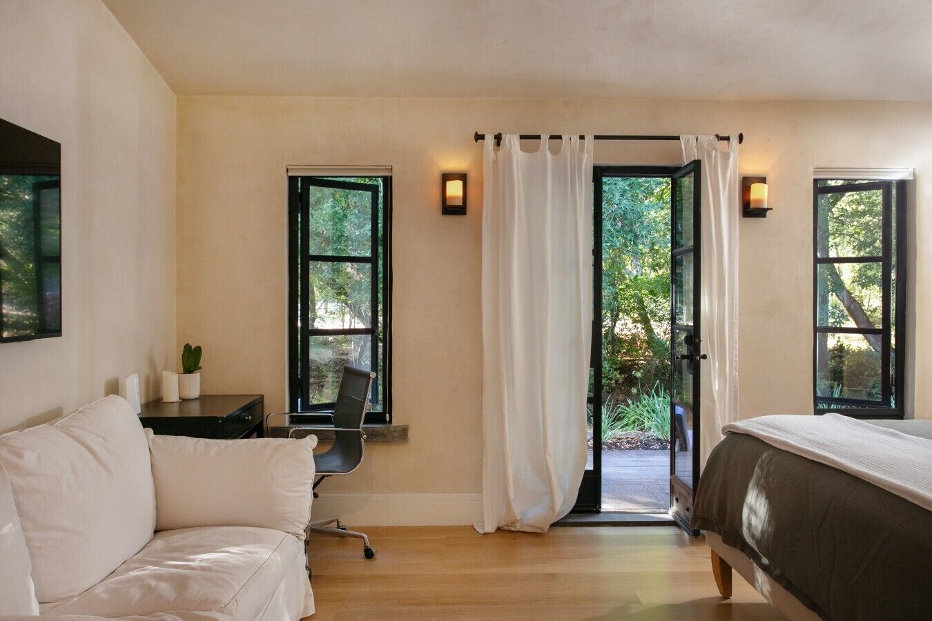 Un dormitorio con cama, escritorio, silla y dos ventanas con cortinas.