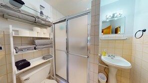A bathroom with a glass shower enclosure, a white sink, and shelves with towels. - Gunni Getaway - Pet Friendly (Gunnison)