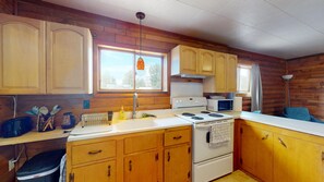 A compact kitchen with wooden cabinets, a stove, a microwave, and a window providing natural light. - Gunni Getaway - Pet Friendly (Gunnison)
