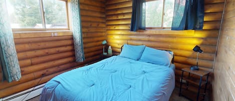 A log cabin bedroom with a bed, two bedside lamps, a nightstand, and curtains.