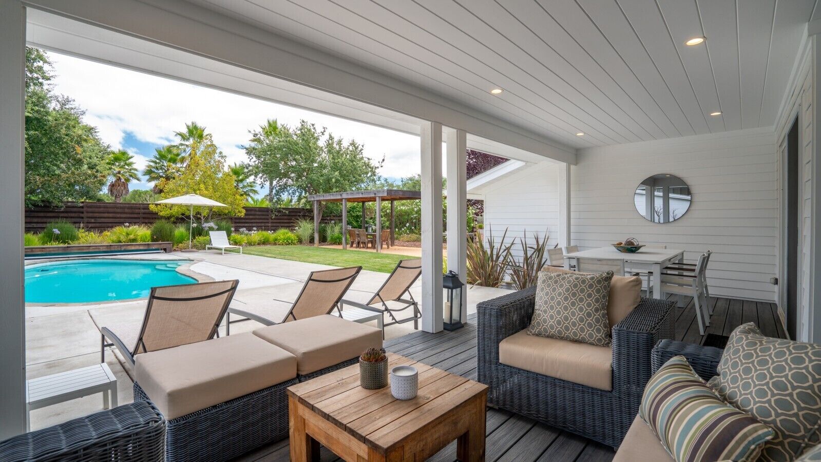 A covered outdoor seating area with a pool, lounge chairs, and a table.