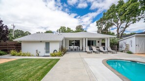 Propiedad residencial con piscina, un porche cubierto con asientos y césped bien cuidado.