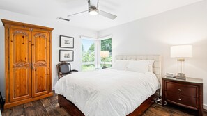 Ein Schlafzimmer mit einem großen Bett, einem Holzschrank, einem Stuhl, einem Nachttisch mit Lampe und einem Fenster mit Jalousien.
