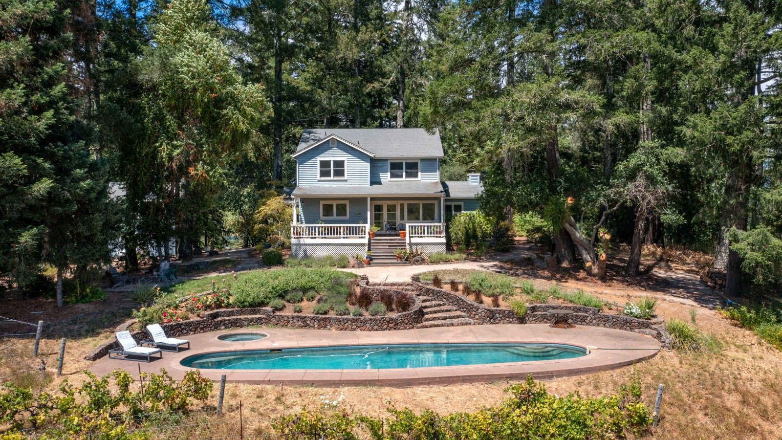 A two-story house with a pool, surrounded by trees and a landscaped garden.