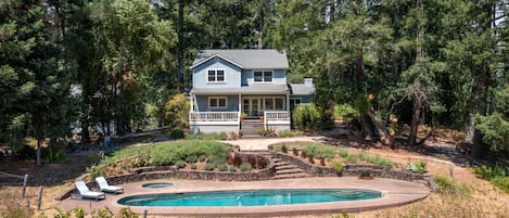A two-story house with a pool, surrounded by trees and a landscaped garden.
