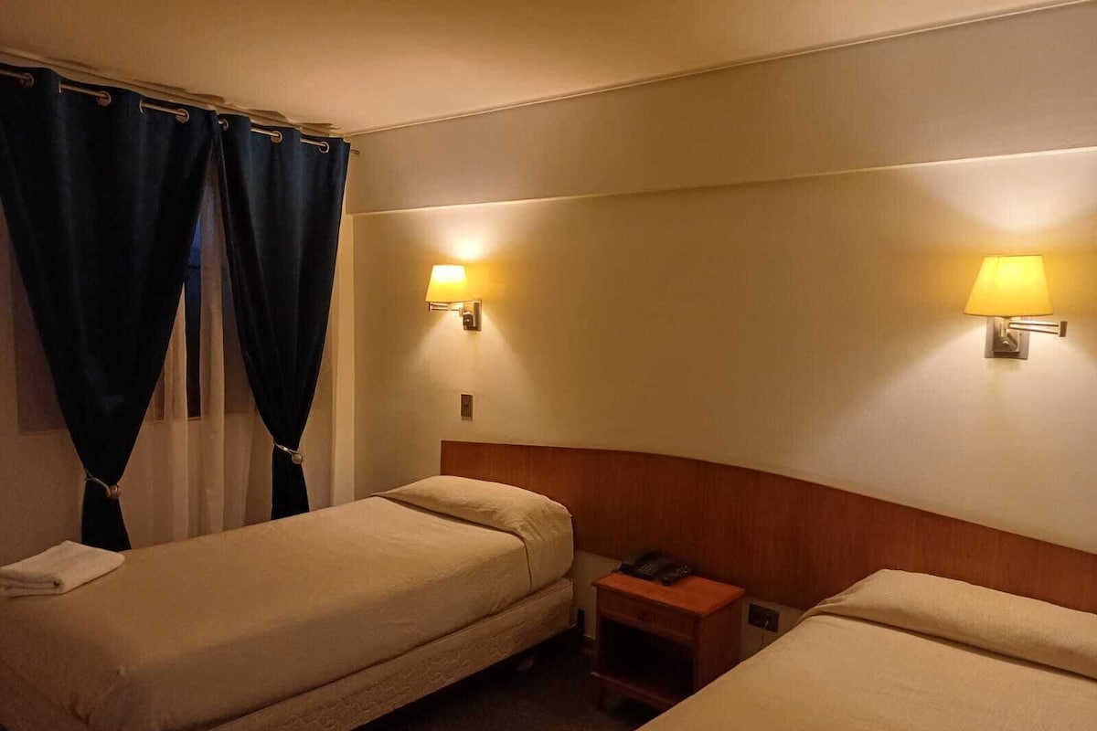 Una habitación de hotel con dos camas individuales, una mesita de noche con teléfono y dos lámparas de pared.