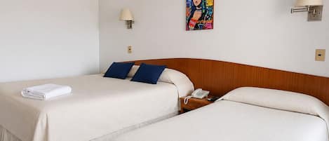 A hotel room with two beds, a wooden headboard, a bedside table with a lamp, a telephone, and a colorful artwork on the wall.