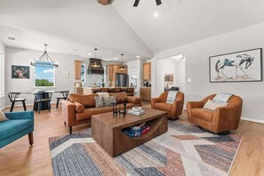 A spacious living area with a modern kitchen in the background, a dining table, and a large window. - Far View Hideout - Hot tub & Fire pit (Fredericksburg)