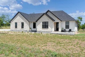 A single-story house with a stone facade, a front porch with seating, and a clear sky. - Far View Hideout - Hot tub & Fire pit (Fredericksburg)