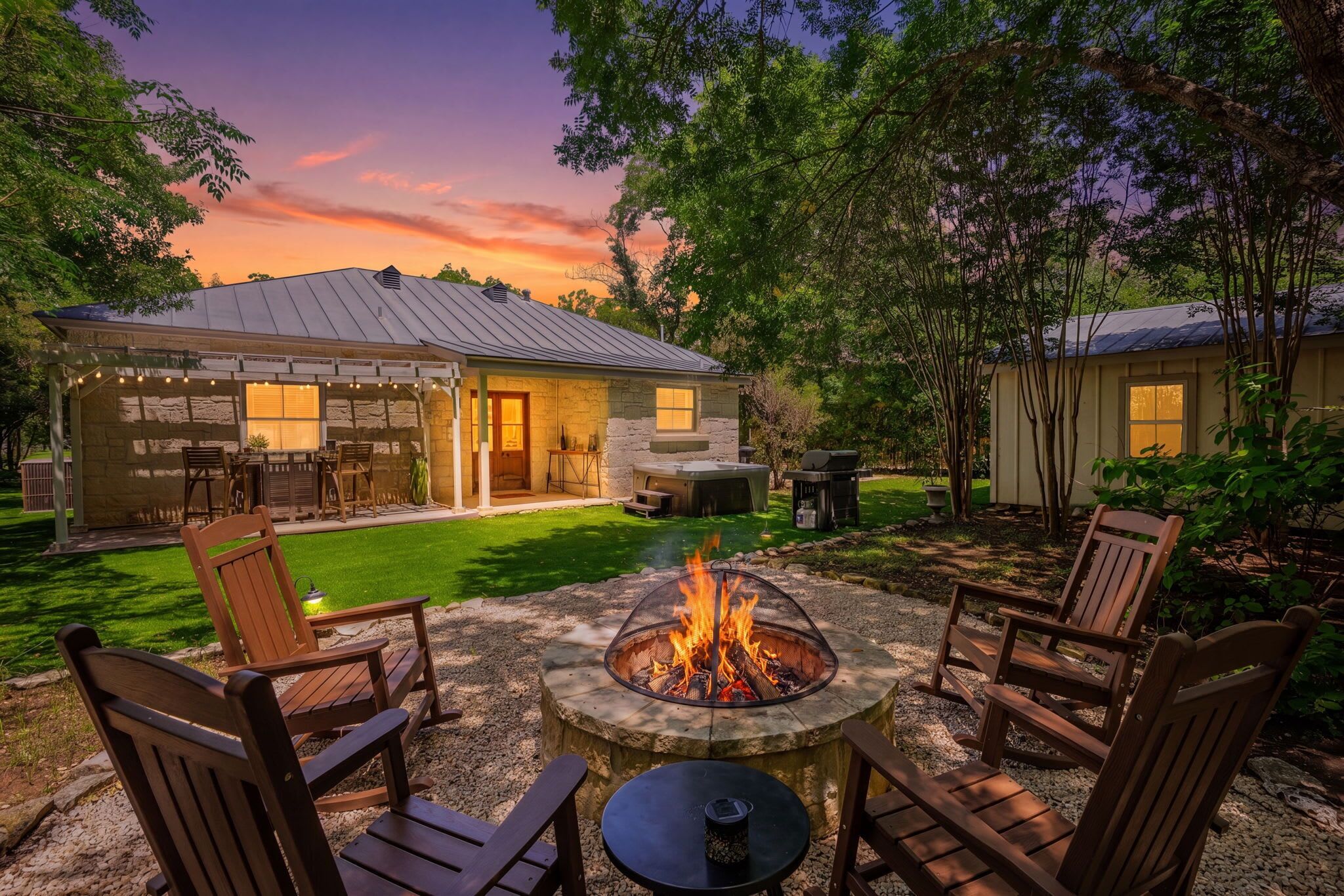 A backyard with a fire pit, outdoor seating, and a stone building.