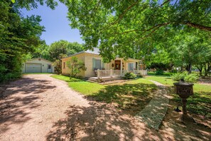 A residential property with a front porch, a garage, and a well-maintained lawn. - Hackberry Haus - Hot Tub (Fredericksburg)