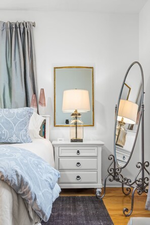 A bedroom with a bed, a bedside table with a lamp, a mirror, and a dresser. - Hackberry Haus - Hot Tub (Fredericksburg)