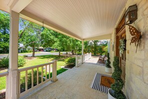 A covered porch with a stone wall, a welcome mat, and a bench. - Hackberry Haus - Hot Tub (Fredericksburg)