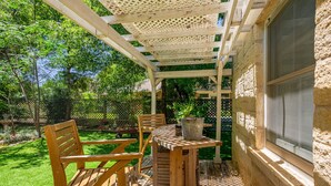 En träaltan med ett bord och stolar, en pergola och en stenmur.