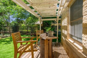 Eine Holzterrasse mit Tisch, Stühlen, einer Pergola und einer Steinmauer.