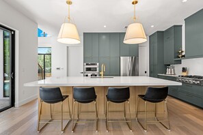 A modern kitchen with a central island, bar stools, stainless steel appliances, and pendant lighting.