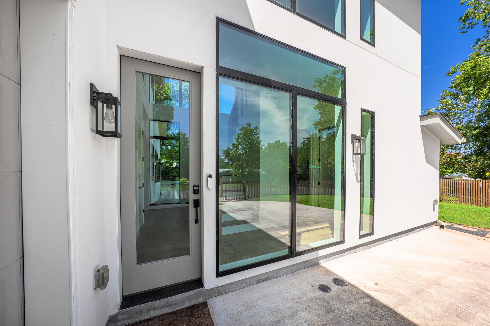 A modern building with large glass doors and windows, a concrete entrance area, and a visible outdoor space with a fence.