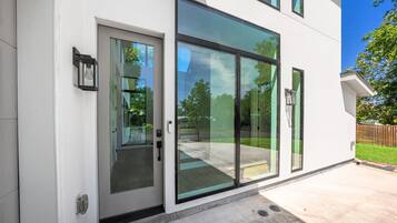 A modern building with large glass doors and windows, a concrete entrance area, and a visible outdoor space with a fence.