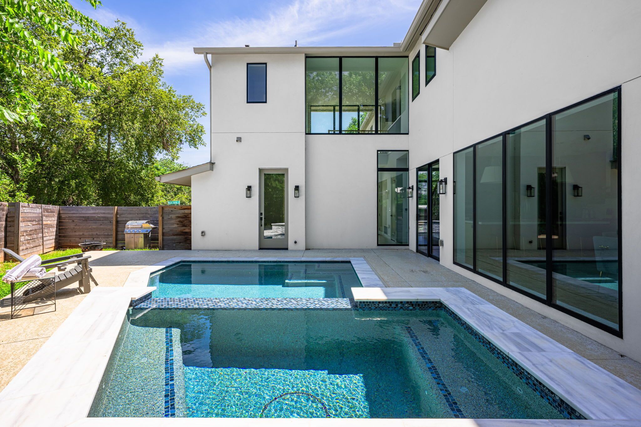 Una casa moderna de dos plantas con piscina, terraza de madera y patio trasero cercado.