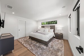 Ein modernes Schlafzimmer mit einem großen Bett, Nachttischen, einem Schreibtisch und einem Fenster mit Blick.