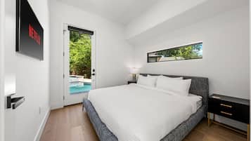 A modern bedroom with a large bed, a bedside table, a nightstand, a wall-mounted TV, and a door leading to a pool area.