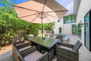 Eine Terrasse im Freien mit Tisch und Stühlen, einem großen Sonnenschirm und einem Pool.