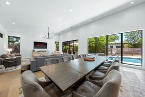 Ein geräumiges Wohnzimmer mit großem Esstisch, bequemen Sitzgelegenheiten, einem Flachbildfernseher und Blick ins Freie.