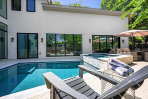 A modern pool area with a clear pool, lounge chairs, and a view of a house with large windows.