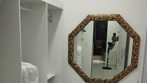 A white wardrobe with shelves and hanging space, a large octagonal mirror with a patterned frame, and a tiled floor. - Edícula 55 M2 aceita pequenos pets (Foz do Iguaçu)