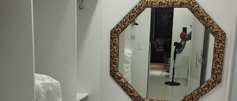 A white wardrobe with shelves and hanging space, a large octagonal mirror with a patterned frame, and a tiled floor.