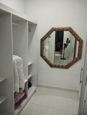 A white wardrobe with shelves and hanging space, a large octagonal mirror with a patterned frame, and a tiled floor.