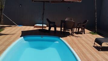 A swimming pool with a wooden deck, a table with chairs, and a large umbrella.