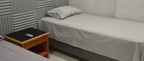 A room with a single bed, a nightstand, and a wall-mounted light switch.
