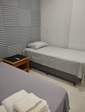 A room with a single bed, a nightstand, and a wall-mounted light switch.