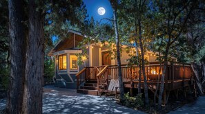 A cabin with a deck, surrounded by trees, and a visible moon in the sky. - Modern Comfort in the Mountains (Big Bear)