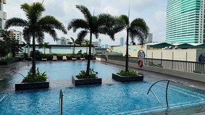 A swimming pool with palm trees, lounge chairs, and a cityscape in the background. - Condo in Araneta City Cubao • Walk to Coliseum • Smart Lock • Parking • Pool (Quezon City)