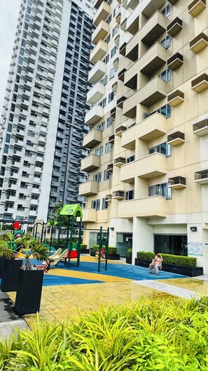 Un immeuble résidentiel doté de nombreux balcons et d’un espace de jeux pour enfants avec des toboggans et des balançoires.