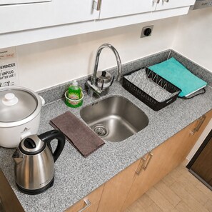 A kitchen with a stainless steel sink, a kettle, a dish soap bottle, a dish rack, and a pot with a lid. - Condo in Araneta City Cubao • Walk to Coliseum • Smart Lock • Parking • Pool (Quezon City)