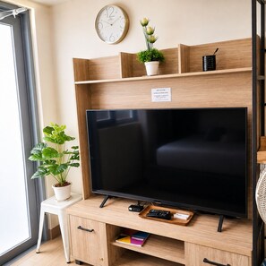 A modern living room with a flat-screen TV, wooden shelves, a potted plant, a small table, and a white chair. - Condo in Araneta City Cubao • Walk to Coliseum • Smart Lock • Parking • Pool (Quezon City)