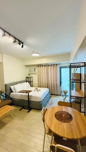 A hotel room with a bed, a desk, a chair, a dining table, and a view of the outdoors.