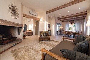 Ein großzügiges Wohnzimmer mit Kamin, eine Essecke mit einer Deckenleuchte und Blick ins Freie.