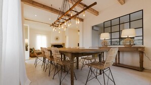 A dining area with a large wooden table surrounded by wicker chairs, a hanging light fixture, and a large window with a view. - Large Country Villa with Swimming Pool in Tuscany (La Chiesa Collegozzi)