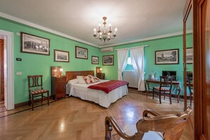 Quarto de hotel com cama, mesas de cabeceira, escrivaninha e cadeiras.