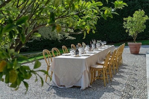 An outdoor dining area with a long table set for a meal, surrounded by chairs, and a potted plant. - Villa Donzella - Luxury historic villa with pool (Menaggio)