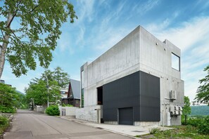 A modern building with a large garage door, surrounded by greenery and a clear sky. - Nero (Abuta)