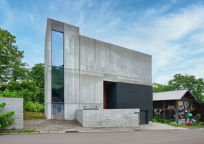 Ein modernes Gebäude mit großen Glasfenstern, einer Betonfassade und einer daran angrenzenden Holzkonstruktion.